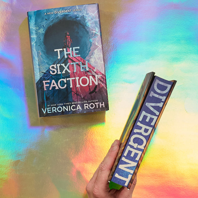 A hand holds a copy of the book 'Divergent' while another copy of 'The Sixth Faction' by Veronica Roth lies on a colorful, iridescent surface.