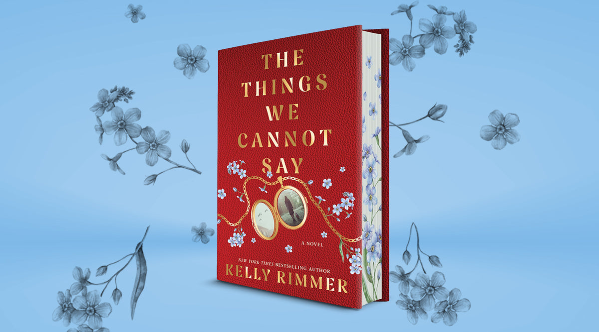 Hardcover of The Things We Cannot Say by Kelly Rimmer, with a red cover, gold lockets, and blue forget-me-not sprayed edges, on a light blue floral background